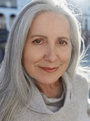 Ángela Rey - Vidente Médium y Guía Espiritual Retrato al natural de Ángela Rey, vidente médium y guía espiritual. Mujer sabia de cabello plateado iluminada por luz natural, experta en sanación de lazos kármicos y limpieza energética.